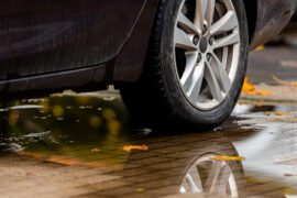 Gros plan sur un pneu arrière de voiture roulant sur une flaque d'eau avec des feuilles d'automne