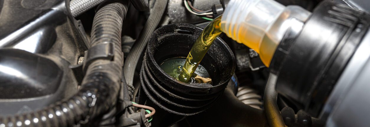 Mécanicien automobile versant de l’huile neuve dans le moteur depuis un bidon en plastique, dans un atelier.