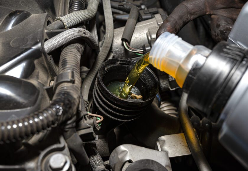 Mécanicien automobile versant de l’huile neuve dans le moteur depuis un bidon en plastique, dans un atelier.