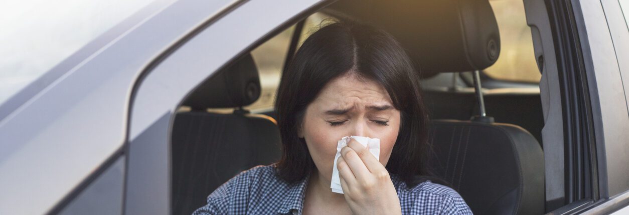 Jeune femme éternuant au volant de sa voiture. Concept de santé, virus, allergie.