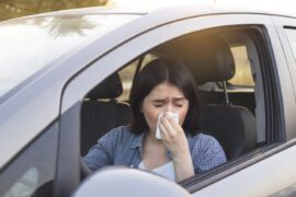 Jeune femme éternuant au volant de sa voiture. Concept de santé, virus, allergie.