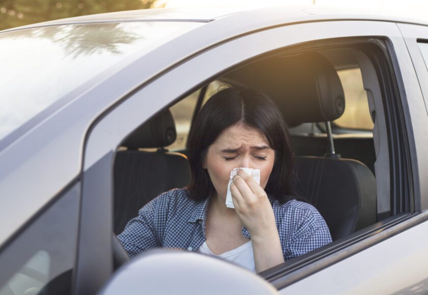 Jeune femme éternuant au volant de sa voiture. Concept de santé, virus, allergie.