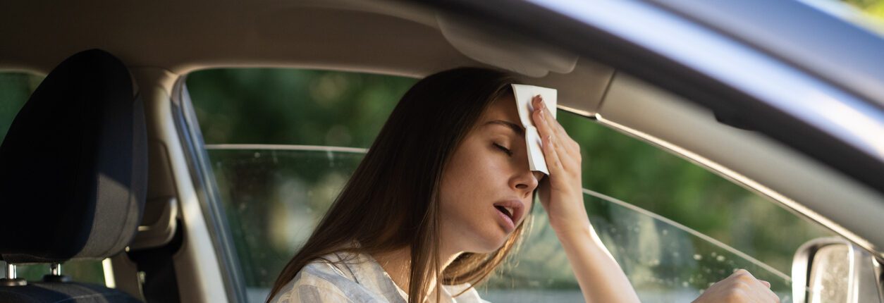 Conductrice ayant chaud pendant une vague de chaleur dans sa voiture, souffrant de la canicule, confrontée à un problème de climatisation défectueuse, s’essuie le front avec un mouchoir. Concept d’été et de forte chaleur.