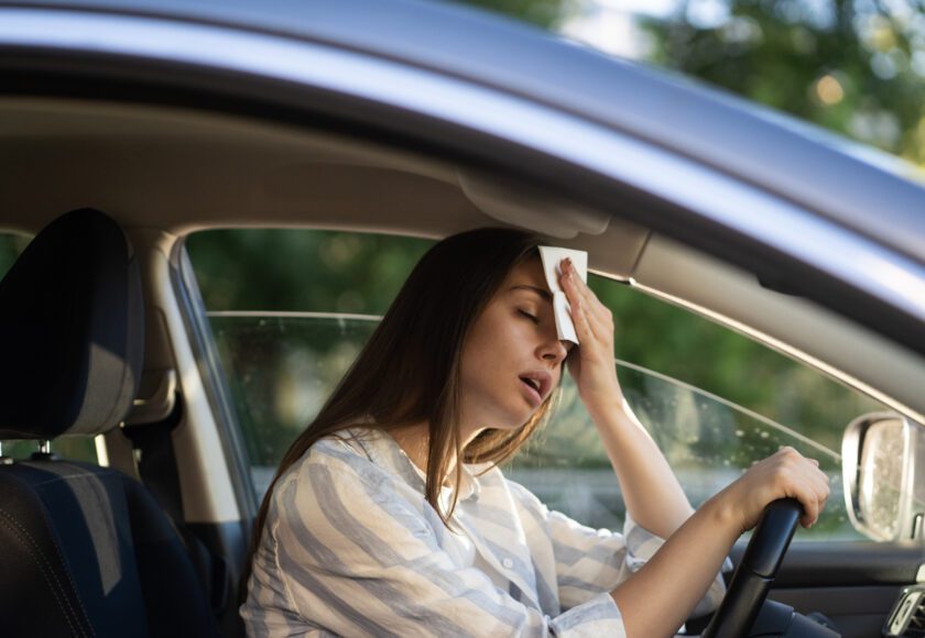 Conductrice ayant chaud pendant une vague de chaleur dans sa voiture, souffrant de la canicule, confrontée à un problème de climatisation défectueuse, s’essuie le front avec un mouchoir. Concept d’été et de forte chaleur.