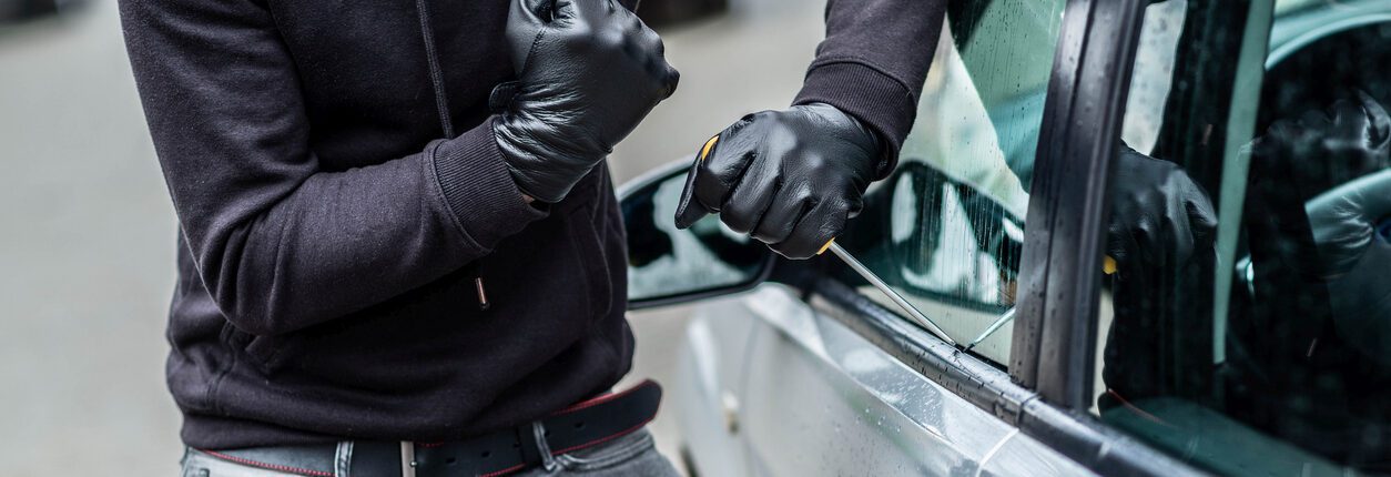 Un homme vêtu de noir, cagoule sur la tête, tente de s’introduire dans une voiture à l’aide d’un tournevis. Concept de vol et de tentative de cambriolage de voiture.