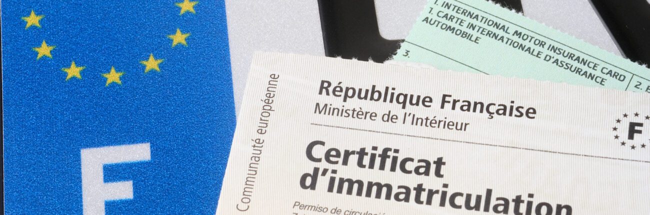 Certificat d'immatriculation (carte grise) avec le papier d'assurance et la plaque d'immatriculation au fond.