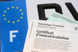 Certificat d'immatriculation (carte grise) avec le papier d'assurance et la plaque d'immatriculation au fond.
