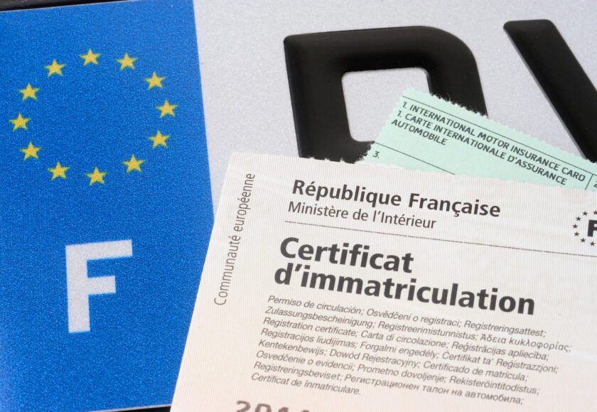 Certificat d'immatriculation (carte grise) avec le papier d'assurance et la plaque d'immatriculation au fond.