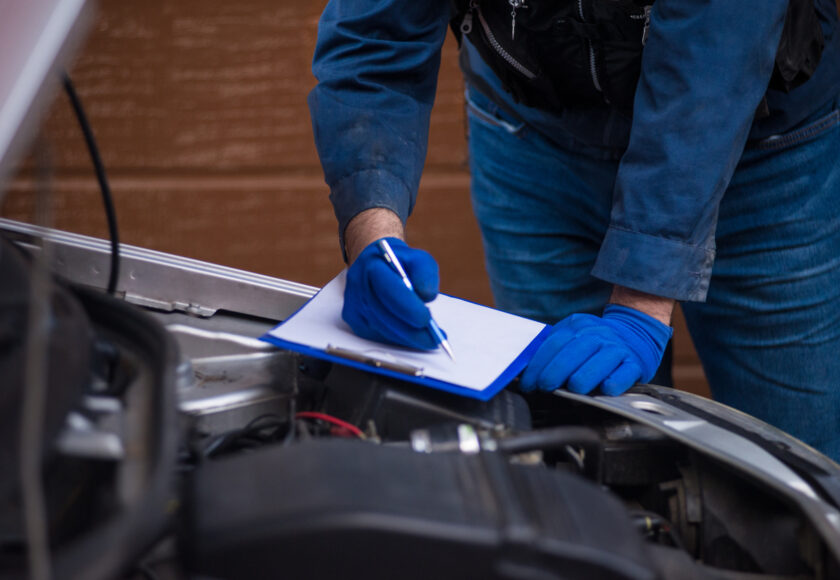 Le capot ouvert, un technicien procède au contrôle d'une voiture standard grise